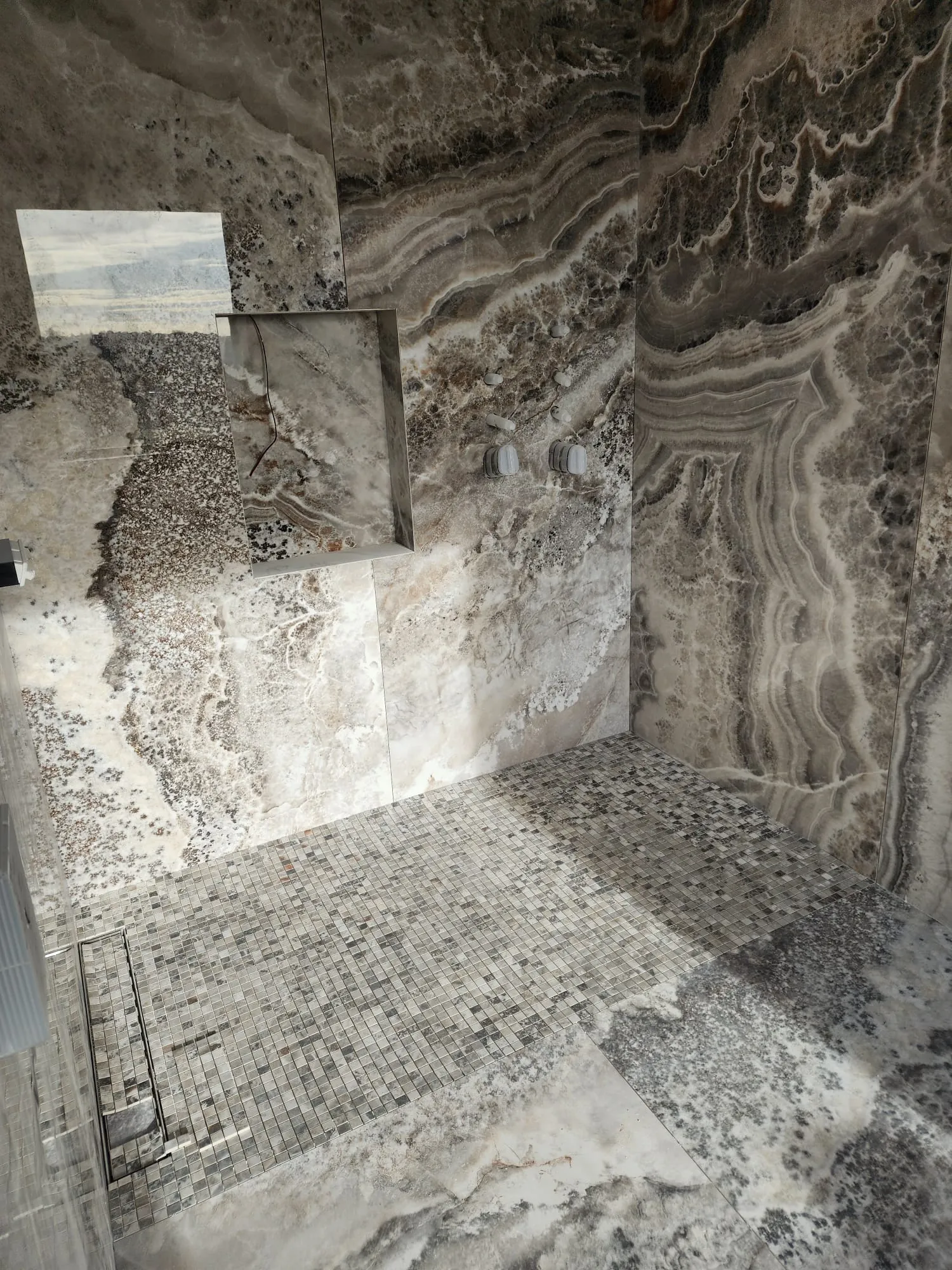 Large format porcelain slab shower walls with a recessed niche and mosaic floor