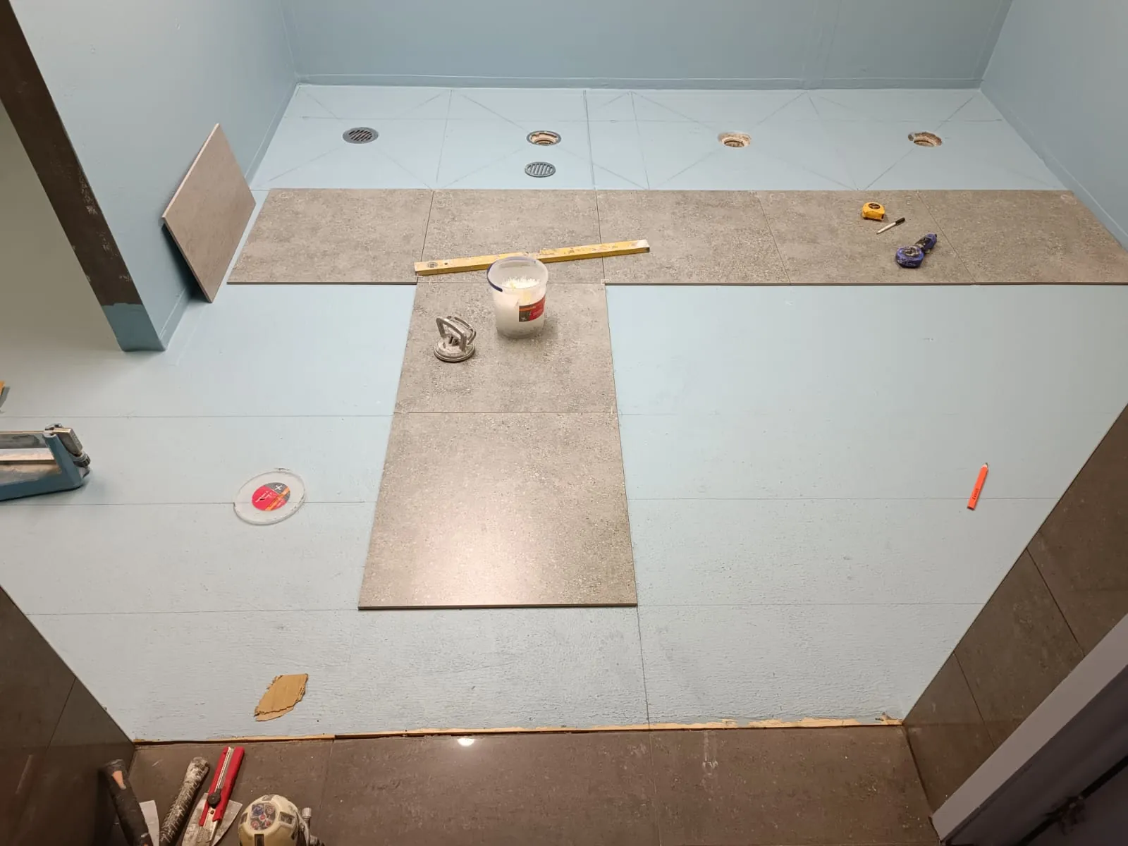 Waterproofed floor and walls around drainage openings, with tiles being set out