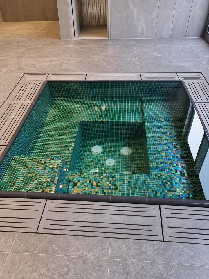 Green and blue mosaic spa basin surrounded by drainage grates